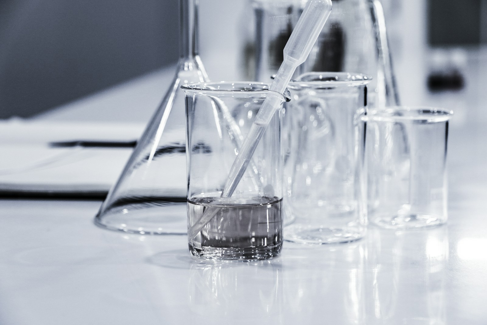 Scientist in gloves analyzing blue liquid in a laboratory setting with microscope and glassware.